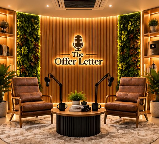 The studio set: two tan leather armchairs with podcast microphones either side of a round fluted table, in front of the logo wall